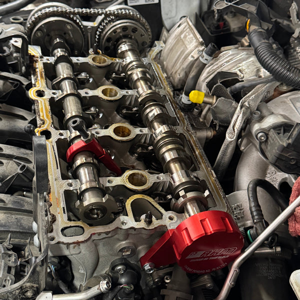 Red AHM cam bridge tool clamped on a VW/Audi EA888 2.0T cylinder head with the cam cover off, camshafts exposed.